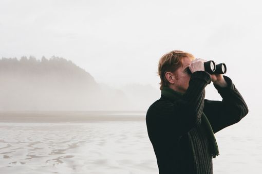 Man looking through binoculars with island in background