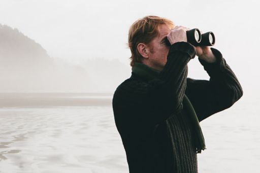 Man looking through binoculars with island in background