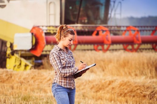 girl in a arable field with a combine harvester behind her