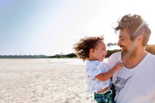 Father and son laughing on the beach at sunset