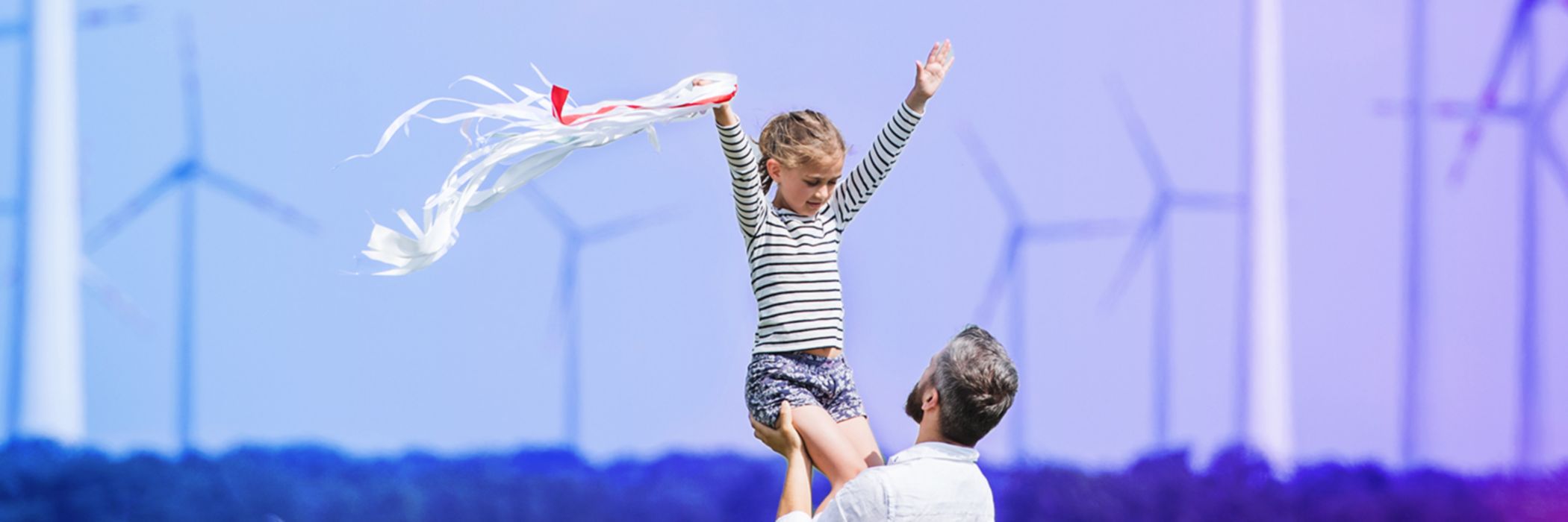 dad lifting daughter daughter in field in front of windturbines