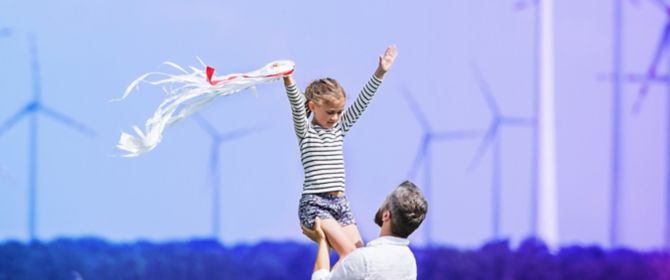 dad lifting daughter daughter in field in front of windturbines