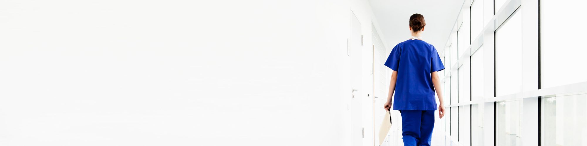 Female doctor walking along white corridor holding clipboard