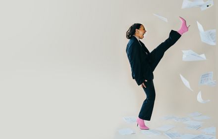 Frau im Anzug streckt Bein nach oben und Papiere fliegen