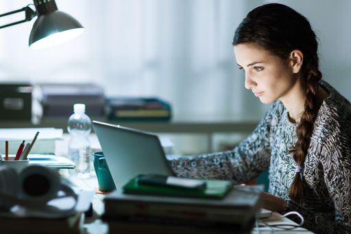 Frau sitzt am überfüllten Schreibtisch vor Laptop