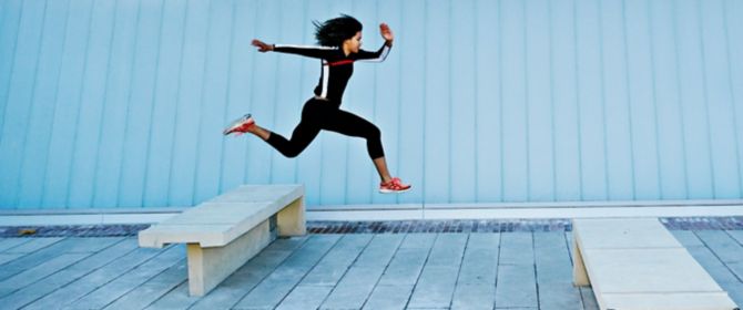 Frau in Sportkleidung springt über Betonbank