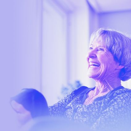 A laughing grey-haired woman relaxes in her home