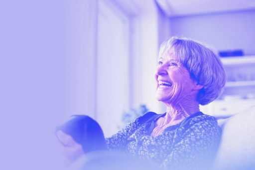 A laughing grey-haired woman relaxes in her home