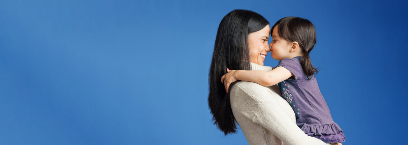 A mother holds her young daughter against a bright blue background