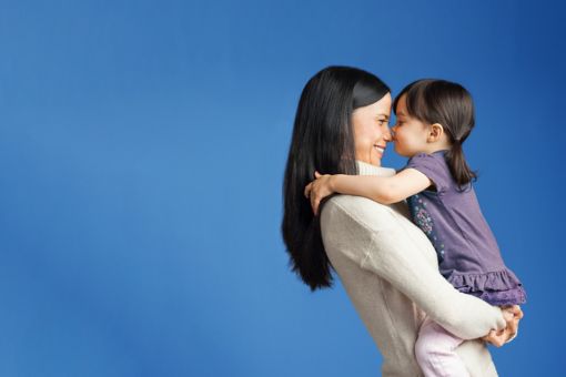 A mother holds her young daughter against a bright blue background