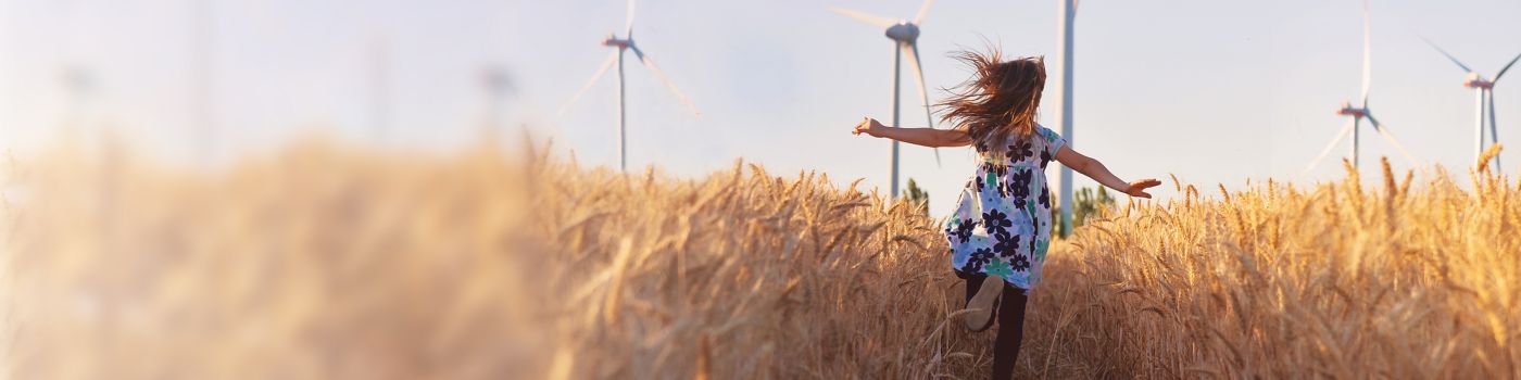 Girl running through field with wind turbines
