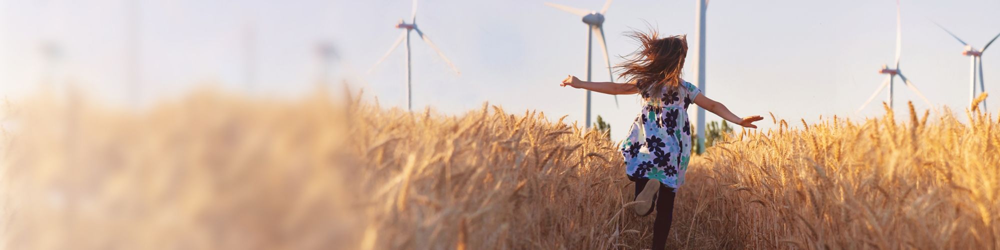 Girl running through field with wind turbines