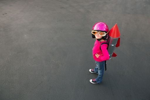 A young girl standing on a road, wearing jeans, a red shirt, and black shoes.