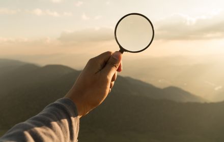 Hand with magnifying glass with landscape behind it