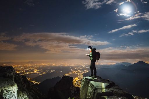 Hiker on top on the mount, full moon and city illuminated