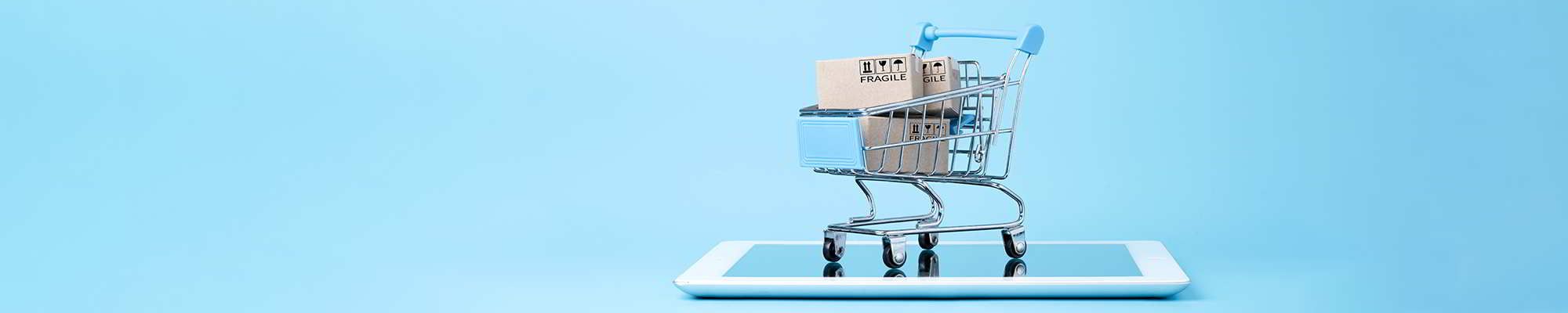 Isolated photo of Shipping paper boxes inside blue shopping cart trolley on tablet with blue background and copy space , Online shopping and e-commerce concept.