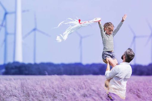 Man lifting child in field with wind turbines in background