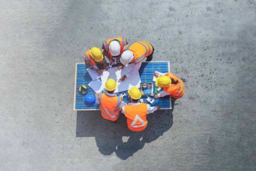 Top view of architect engineer working on solar panel and his blueprints with solar photovoltaic equipment and wind turbine on construction site.