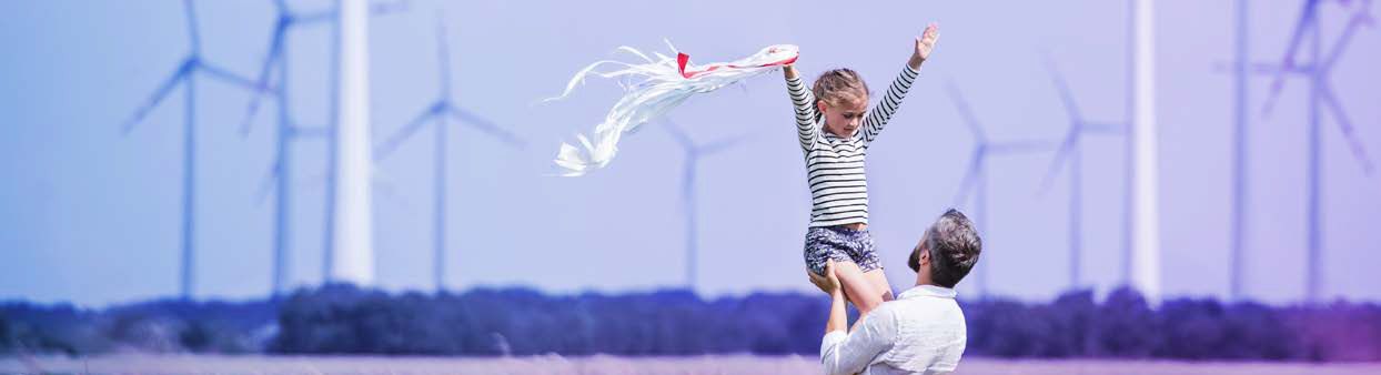 Dad lifting daughter in field with wind turbines in background