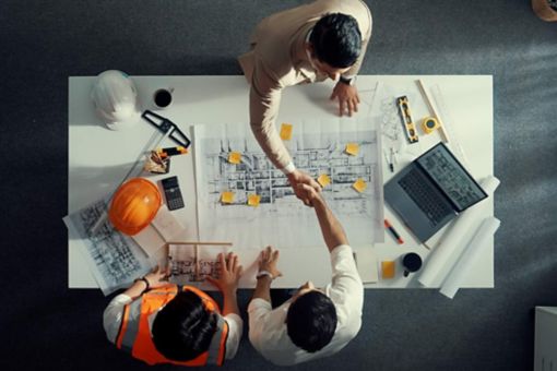 Architect and construction workers shaking hands over building plans