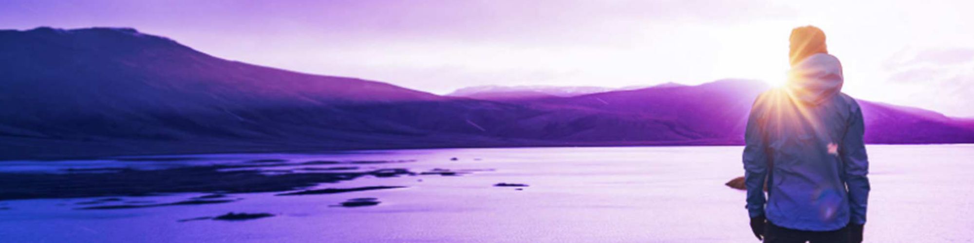 Person on shore looking out at mountains and sea