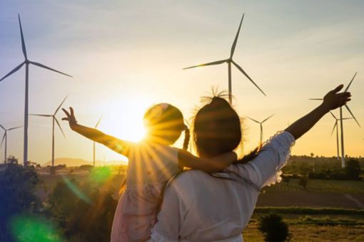 Woman and child in field with wind turbines at sunset