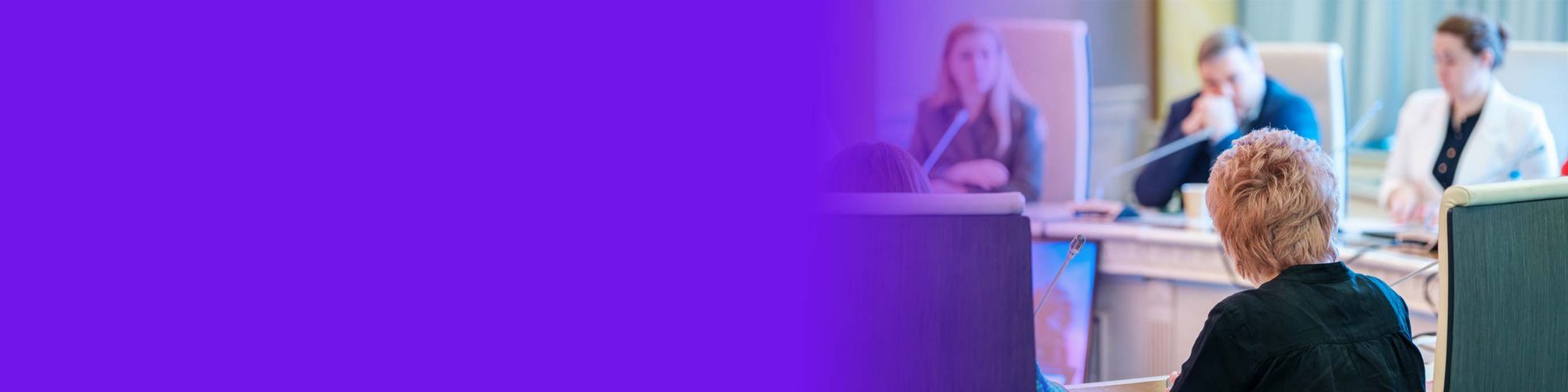 Back view of unrecognizable businesswoman sitting at round table near colleagues with microphones during conference in spacious hall