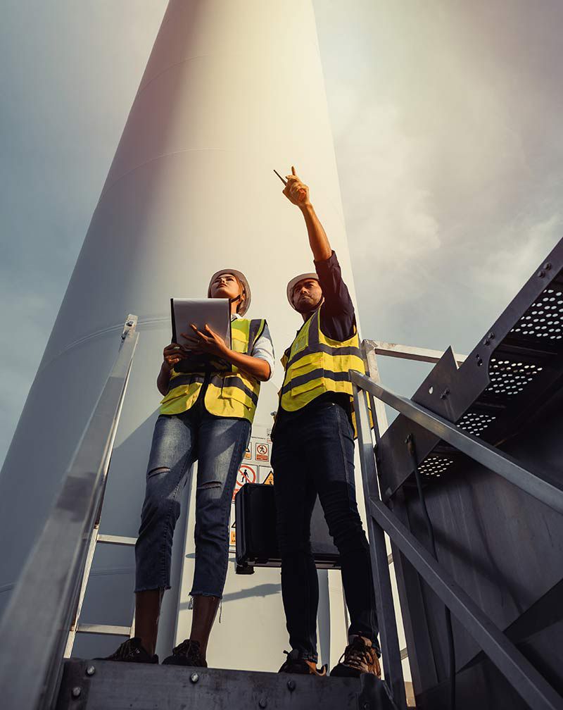 Young man and woman maintenance engineer team working and holding the report in wind turbine farm. Generator station, renewable energy