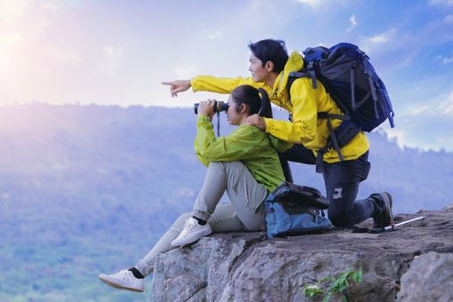 People sitting on a cliff, looking into binoculars at a scenic view