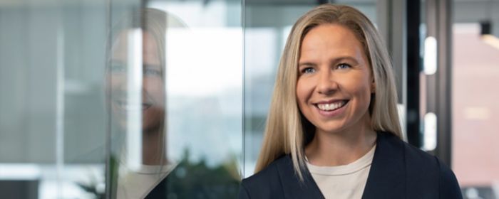 Ung ljóshærð kona horfir fram fyrir sig og brosir breitt með skrifstofu KPMG í Borgartúni í bakgrunni