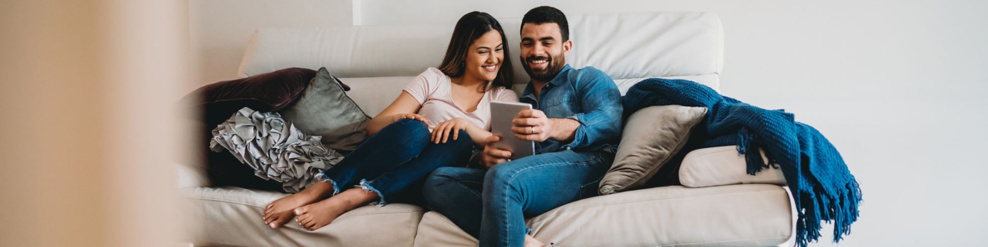 Pareja de jóvenes sentados en el sofá usando una tableta juntos