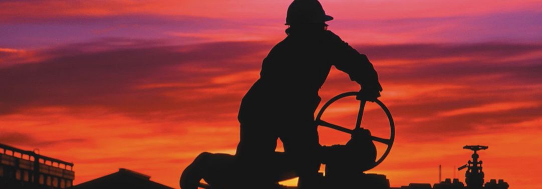 man turning oil gas valve at sunset