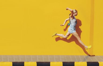 Frau springt vor gelber Wand