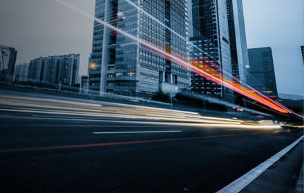 Long exposure of car's light trails on busy road besides huge glass buildings