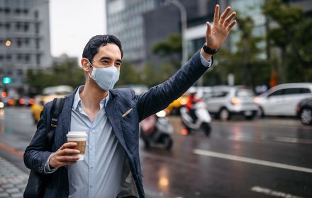 Man in mask waiving hand at taxi holding coffee