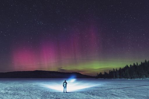 Man standing on frozen lake shining torch at shoreline