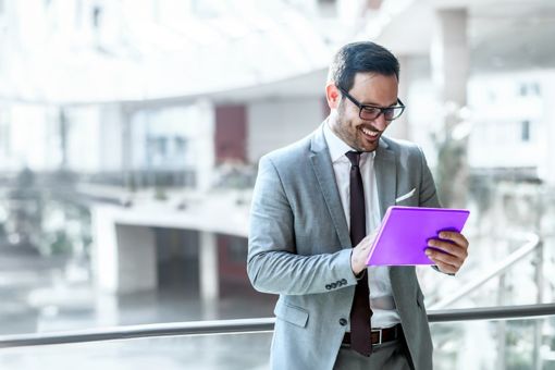 Man smiling whilst looking down at a tablet in an indoor open space