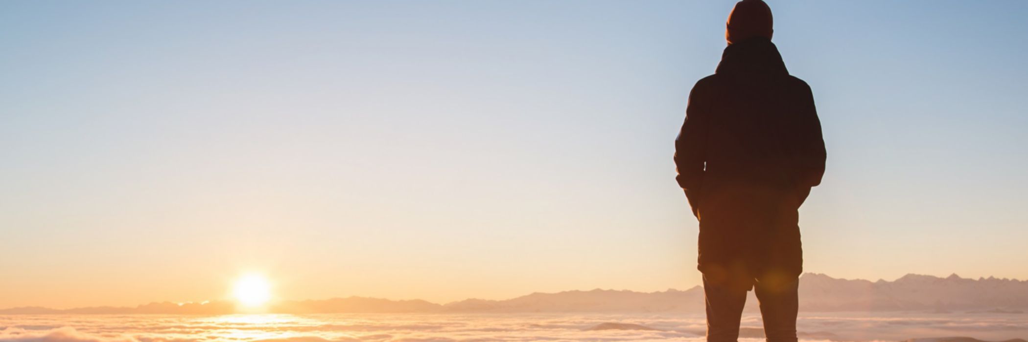 Man standing on mountain peak watching sunset