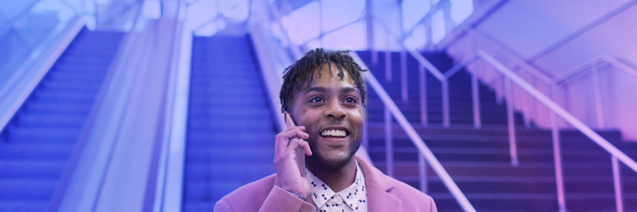 Young businessman talking on smartphone moving down train station escalator