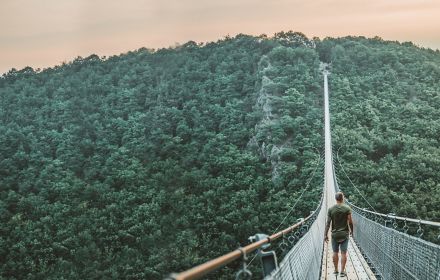 Man walking on bridge through green mountains