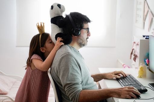 Man working on computer while his daughter is playing