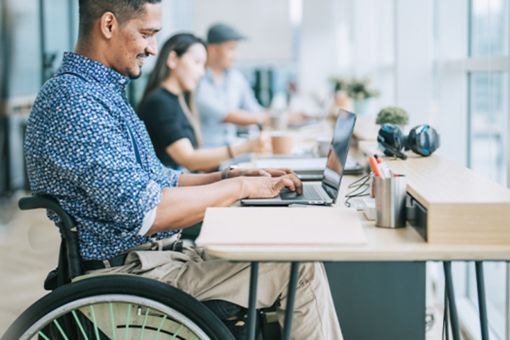 Mann im Rollstuhl arbeitend am Laptop