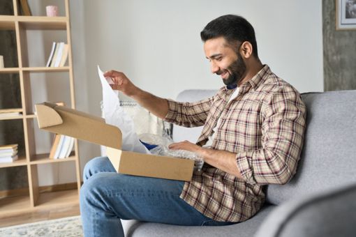 Man sat on a sofa opening a cardboard box