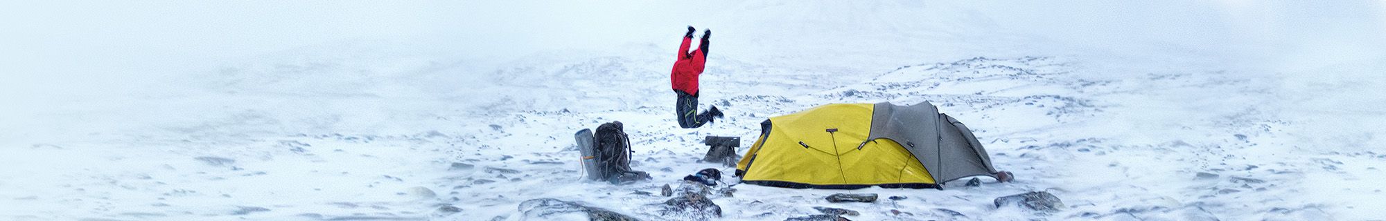 Person jumps in front of tent on a mountain