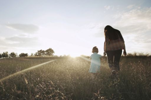 Mom and child walking through a wheat field at sunrise