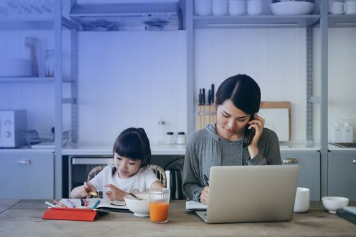 Mutter sitzt telefonierend neben Kind und arbeitet an Laptop