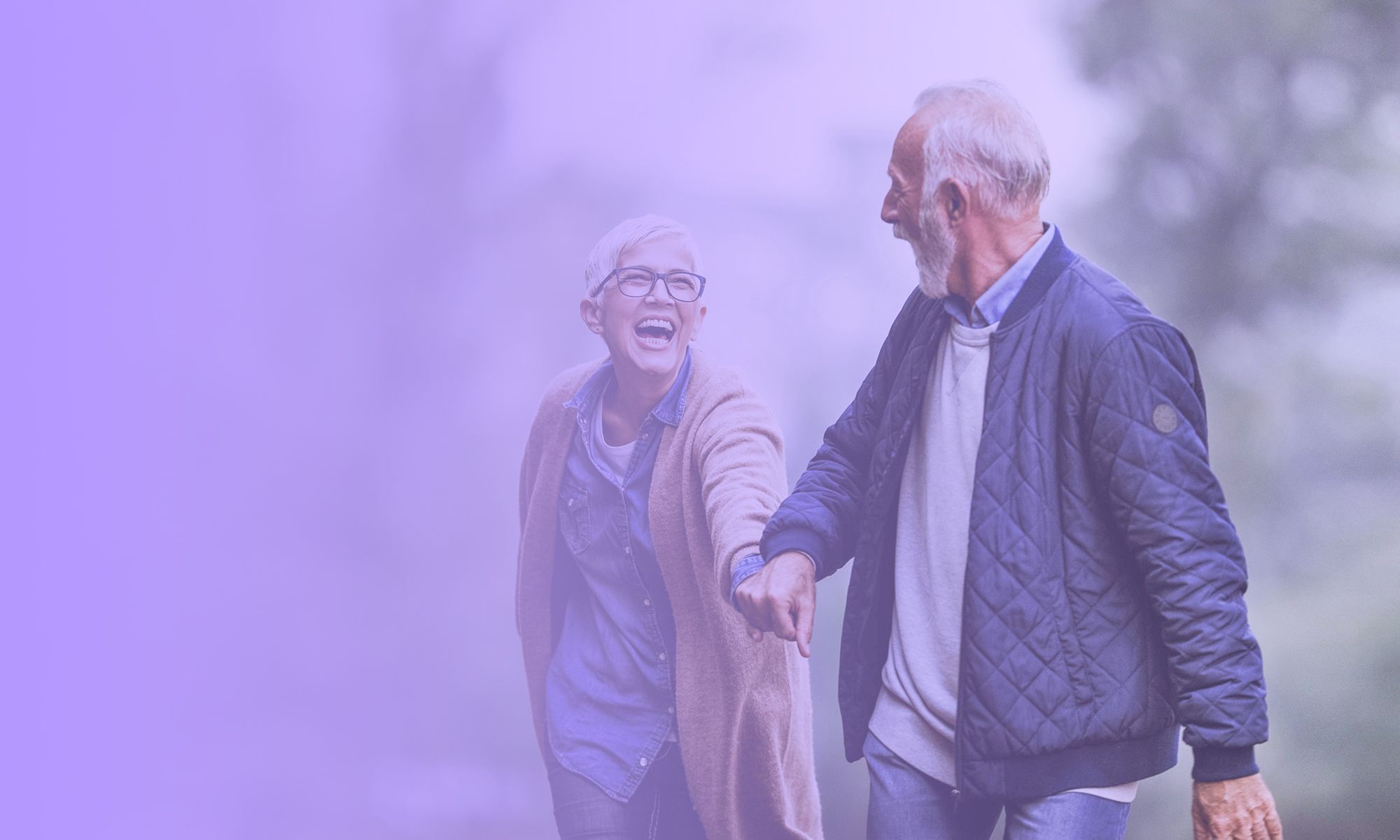 An older couple laughing while walking through a park