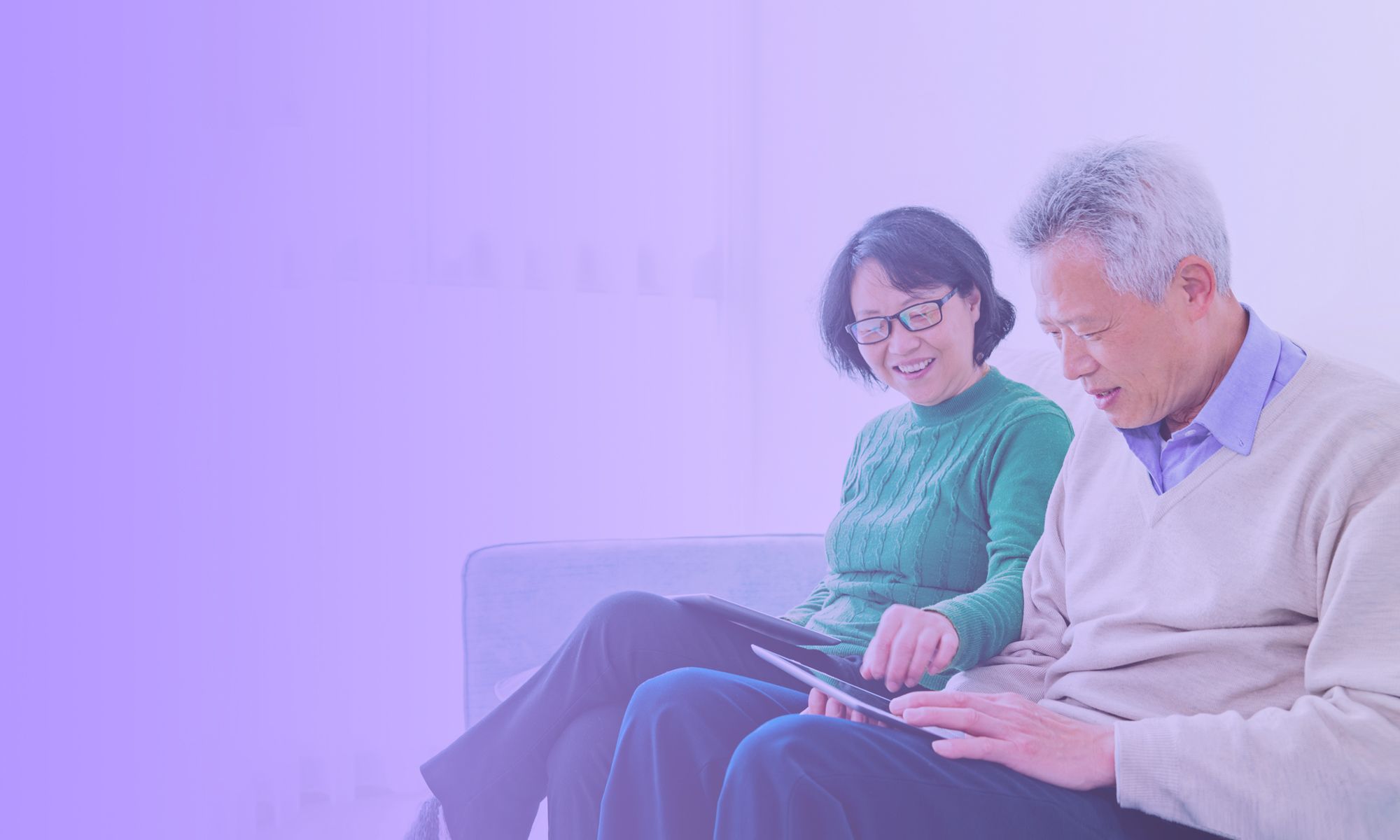 An older couple sit on their couch using a tablet