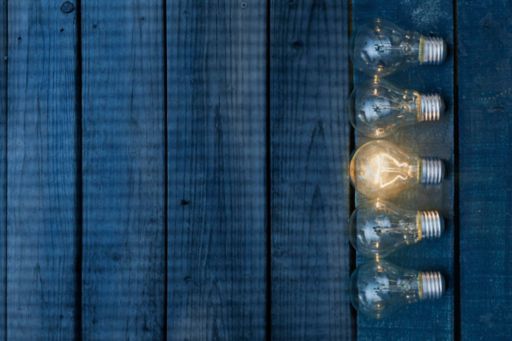 One illuminated bulb among five on blue wood