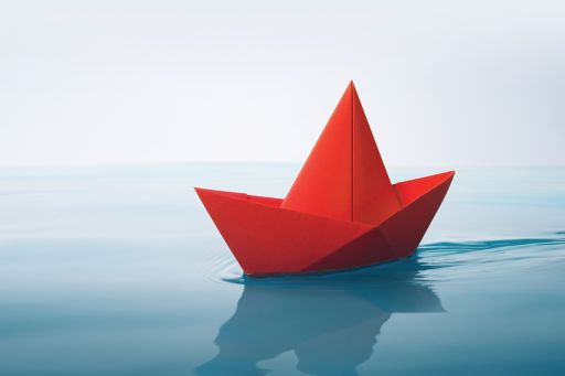 red paper boat sailing on water with waves and ripples